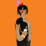 A doll is wearing black and has a pink bow on her head.